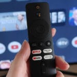 a remote held in a hand with the google tv interface on a screen in the background